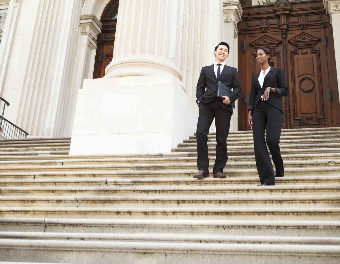 Two business professionals walking down courthouse steps, representing companies seeking outside general counsel support for managing legal risks during growth.