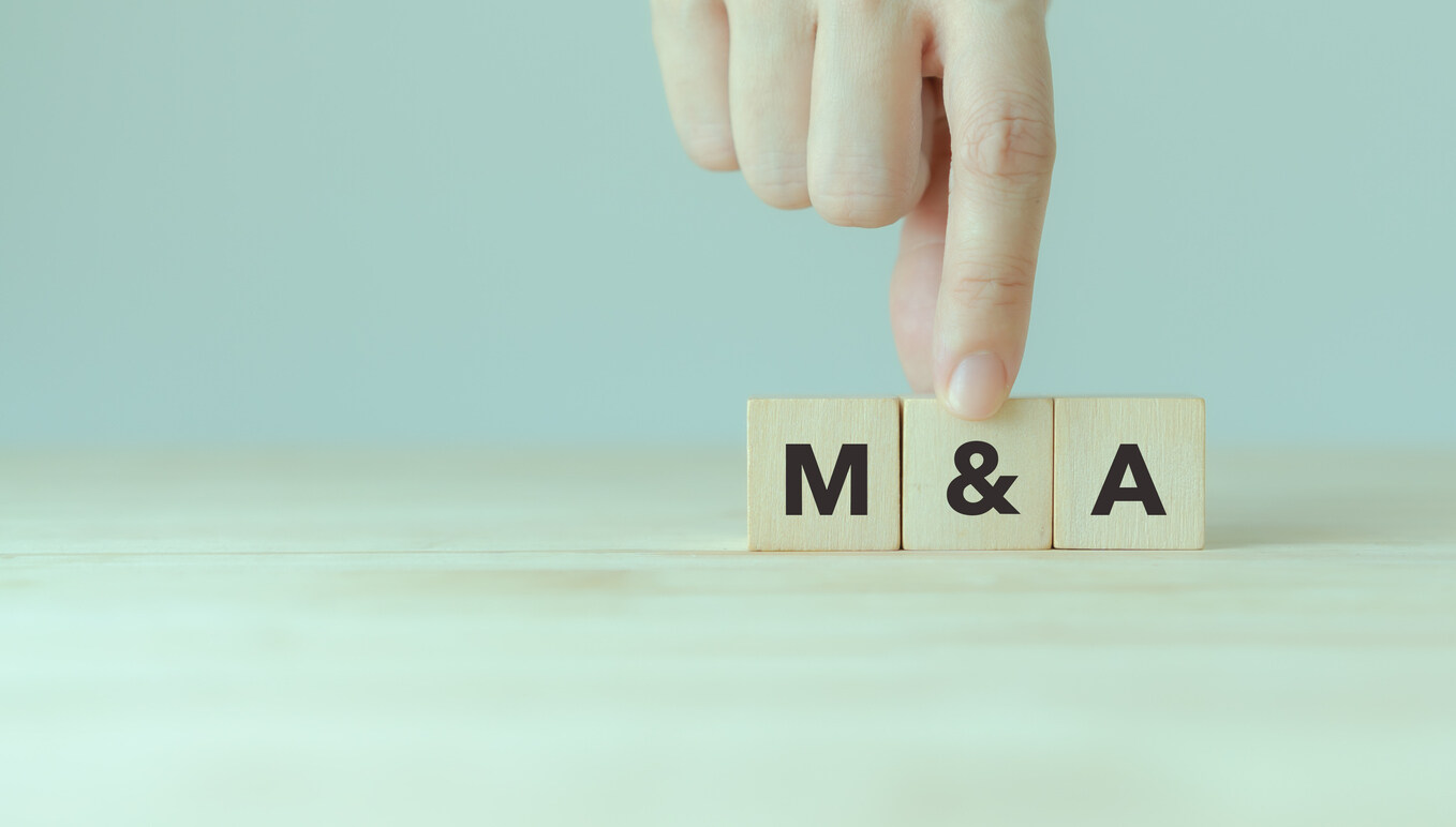 Hand adjusting wooden blocks with 'M&A' letters, symbolizing the strategic importance of deal structure and legal strategy in preserving leverage during M&A negotiations.